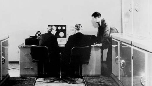 Περιγραφή: Ο Alan Turing με δύο συναδέλφους και έναν υπολογιστή Ferranti τον Ιανουάριο του 1951. Τούρινγκ είχε ήδη ασχολούνται με την κατασκευή τόσο του Κολοσσού και, αργότερα, την αυτόματη υπολογιστική μηχανή.